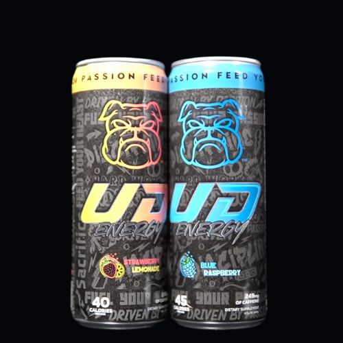 Two cans of UD Energy Drink side by side, one in Strawberry Lemonade and the other in Blue Raspberry flavor, both featuring vibrant bulldog logos and the slogan "Fuel Your Passion, Feed Your Beast". The cans are set against a dark background, highlighting the colorful designs and flavor-specific accents, representing the brand&