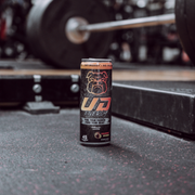 A UD Energy performance drink can in a gym setting, placed on the floor near weightlifting equipment. The can features a bold bulldog logo with the text "Fuel Your Passion, Feed Your Beast," promoting 45 calories and a no-sugar formula, embodying the strength and focus required for intense workouts.